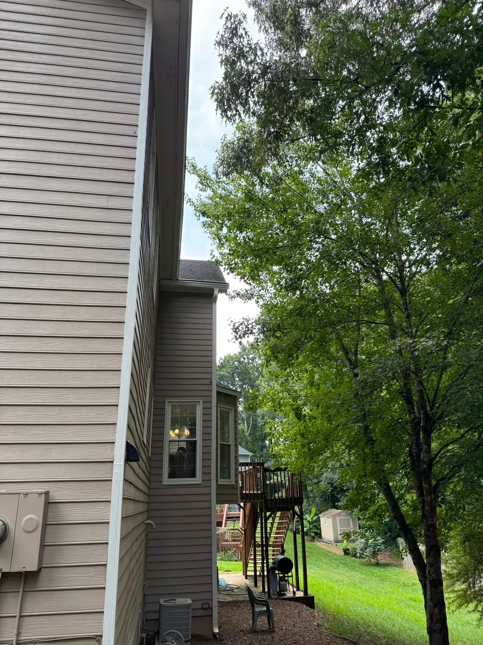 Before: Trees growing toward side of house near roofline and gutters with deck visible in Marietta GA